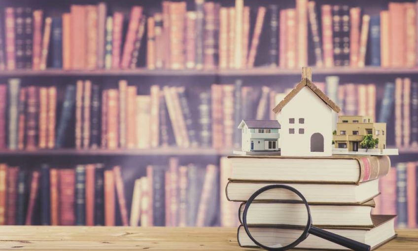 houses sat on top of books with a magnifying glass in the foreground, bookshelves are in the background