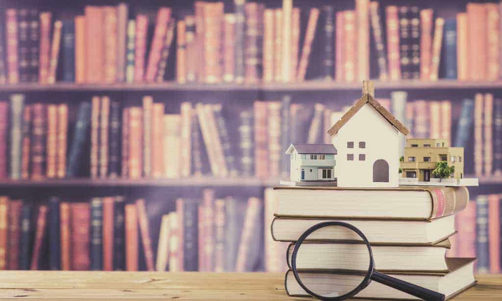 houses sat on top of books with a magnifying glass in the foreground, bookshelves are in the background