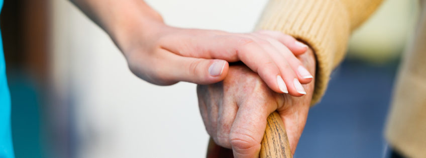 carer holding an elderly person's hand as they grip onto a walking stick