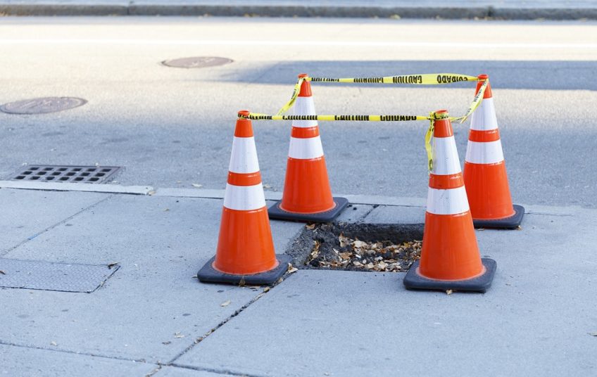 pothole on the sidewalk fenced. traffic cones and cordon type around the hole on the pavement