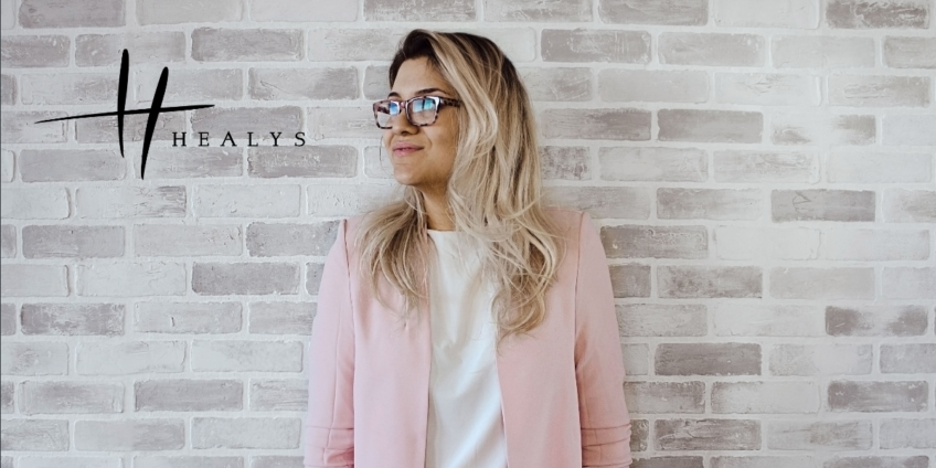 image of a woman wearing a pink business jacket standing in front of a brick wall looking positive