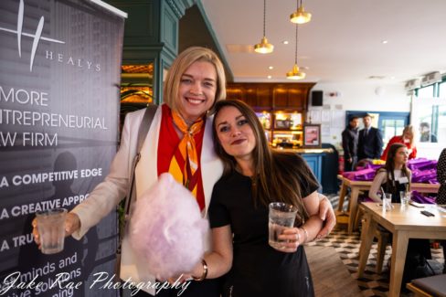 image of two female event attendees standing together and smiling while holding drinks and candy floss