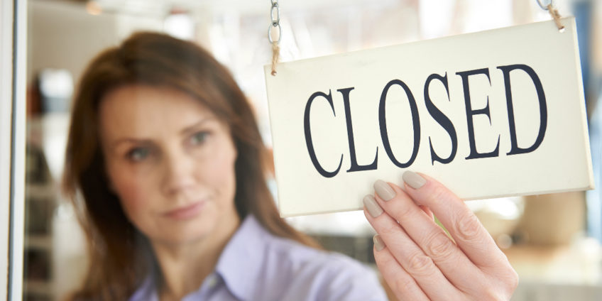 Woman turning shop sign to closed through window