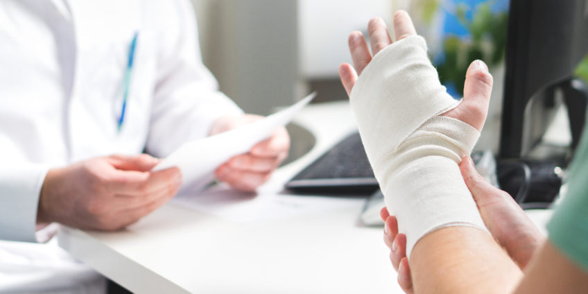 Patient with bandaged hand speaking to doctor at desk