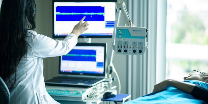 female doctor working on medical equipment while female patient lies next to her inhospital bed