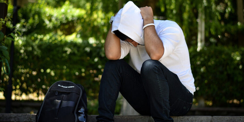 man wearing hood crouched on a wall with his head between his hands