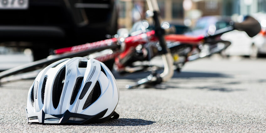 bike fallen on the ground under the wheel of a vehicle in the background of a bicycle helmet which is also sat on the ground