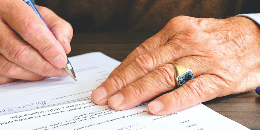 close up of elderly man's hand signing documents